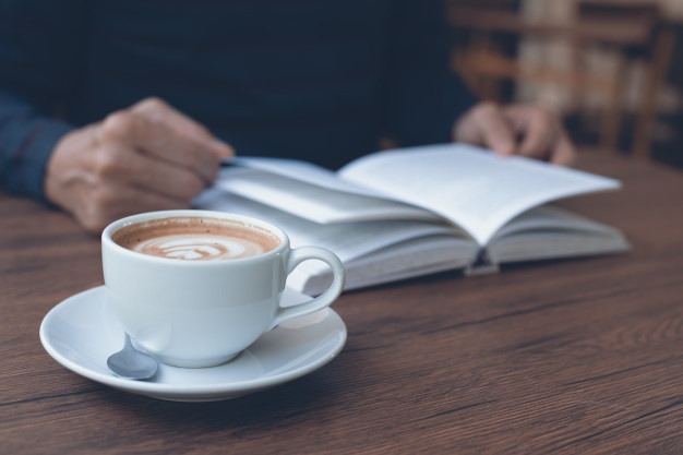 Taza de café en la mesa de madera con un hombre leyendo libro